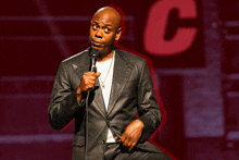 a man in a suit is speaking into a microphone in front of a large letter c