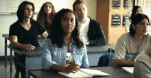 a girl in a denim jacket sits at a desk in front of a white board with the word problem on it