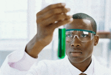 a man wearing safety glasses looks at a green liquid in a beaker