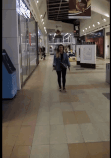 a woman walking down a hallway in a mall with a sign that says ' domino 's ' on it