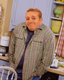 a man in a plaid shirt stands in a kitchen