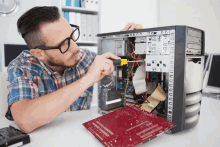 a man wearing glasses is working on a computer with a screwdriver