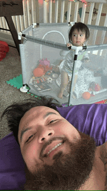 a man with a beard is laying on a bed next to a baby in a crib