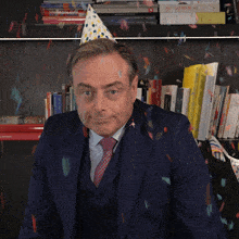 a man wearing a party hat stands in front of a bookshelf with a book titled a valentine 's day