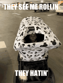 a baby is sitting in a stroller with a mickey mouse canopy and the caption they see me rollin '