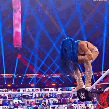 a female wrestler with blue hair is kneeling down in front of a crowd and a sign that says the next thing