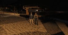 a man and a woman are standing on the beach at night