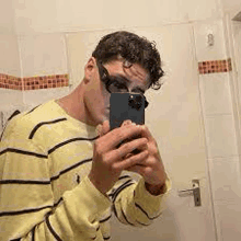 a man is taking a selfie in a bathroom with his phone .