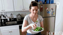 a woman is eating a salad in a kitchen with a sign that says what it is on the refrigerator