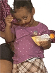 a little girl wearing a purple shirt and plaid skirt is holding a box of food .