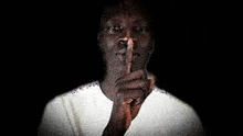 a man in a white shirt is making a silence gesture with his finger to his mouth .