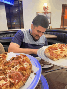 a man sitting at a table eating a pizza with a tv behind him that says ' fox ' on it