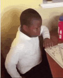 a young boy is sitting at a desk with his eyes closed and a bottle of water in the background .