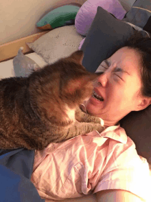 a woman laying on a bed with a cat on her shoulder