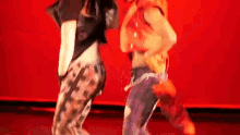 two women are dancing on a stage in front of a red background .