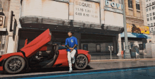 a man leans against a red sports car in front of a movie theater advertising sequel