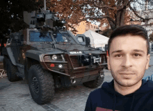 a man taking a selfie in front of a military vehicle with a license plate that starts with i