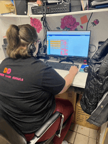 a woman wearing a dunkin donuts shirt sits at a desk with a computer