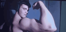 a shirtless man is flexing his muscles in front of a computer screen while wearing headphones .