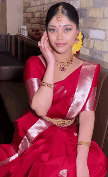 a woman wearing a red saree and gold jewelry holds her hand to her face