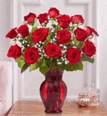 a vase filled with red roses and baby 's breath is sitting on a wooden table .