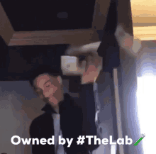 a man in a suit is standing under a table with the words " owned by #thelab " written below him