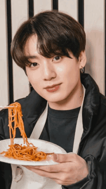 a young man is holding a plate of noodles with chopsticks in his hand