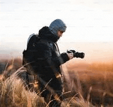 a man is standing in a field holding a camera and taking a picture .