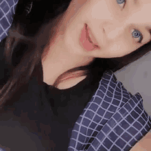 a close up of a woman 's face with blue eyes wearing a black shirt and a plaid shirt .