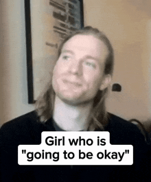 a man with long hair is sitting in front of a wall with a sign that says girl who is going to be okay .