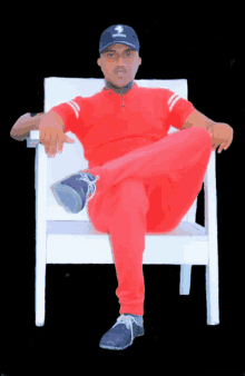 a man in a red shirt is sitting on a white chair with his legs crossed