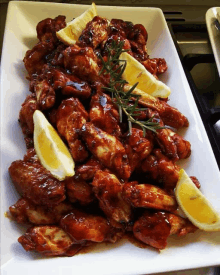 a plate of chicken wings with lemon slices and rosemary on top