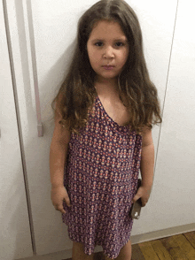 a little girl standing in front of a white cabinet wearing a purple dress