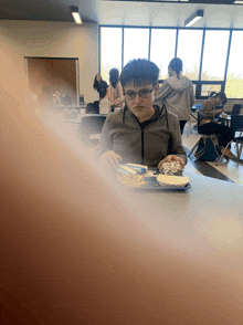 a boy wearing glasses sits at a table with a plate of food in front of him