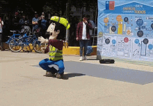 a man in a yellow vest is dancing in front of a sign that says cuando bien energia somos tu ganamos todos