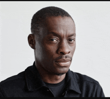 a man in a black shirt looks at the camera with a serious look on his face