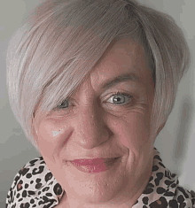 a woman with short white hair and a leopard print shirt is smiling .