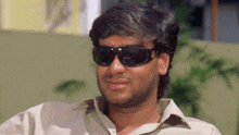 a man wearing sunglasses and a tan shirt is smiling and looking at the camera .