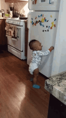 a baby in a diaper stands in front of a refrigerator that has a sticker on it that says " happy birthday "