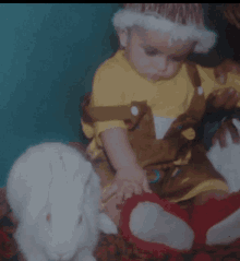 a baby wearing a yellow shirt is playing with a white rabbit