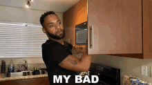 a man in a black shirt is standing in a kitchen with the words " my bad " above him