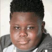 a close up of a young boy 's face with a gray sweater on .