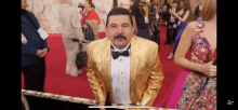 a man in a gold tuxedo and bow tie is standing on a red carpet