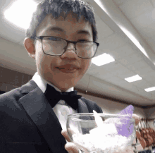 a young man in a tuxedo and bow tie is holding a glass filled with ice cream