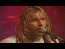 a man with long blonde hair is singing into a microphone .