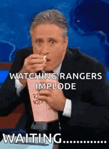 a man in a suit is eating popcorn and watching rangers implode while waiting .