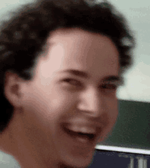 a close up of a man 's face laughing with a blackboard in the background