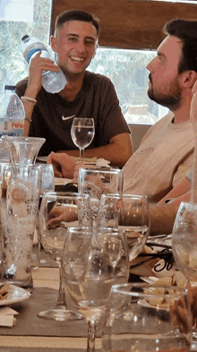 two men sitting at a table with a bottle of perico water