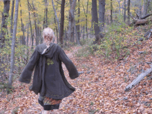 a woman wearing a hooded jacket with a flower on the back walks through the woods