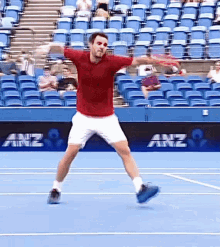 a man in a red shirt is swinging a tennis racquet on a tennis court with anz in the background